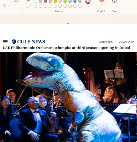 A performer in a large blue and white dinosaur costume on stage with orchestra members and instruments in the background during a concert performance.